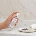 100 % Pure Hemi-Squalane Facial Oil - Close-up of a hand holding a ShaRique 100% Hemi-Squalane Facial Oil bottle with a clear oil drop at the pump, set on a marble bathroom counter.